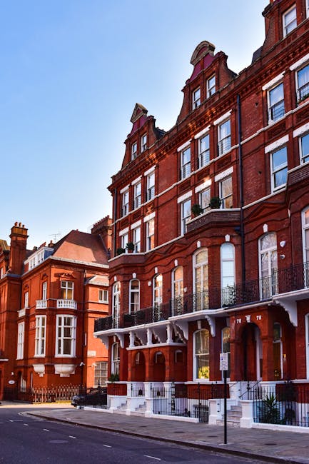 Exterior view of a multi-story residential house with a brick façade and decorative white window frames, situated in East Dulwich SE22. The house features large bay windows on each floor, with some windows having shutters, and a sloped tiled roof with dormer windows. The front garden includes bushes and small trees, with a pathway leading to the white front door. The scene is captured in bright daylight, showcasing the clean and well-maintained appearance of the property. Carpet Cleaners Dulwich, a professional cleaning service, emphasizes interior surface cleaning and deep sanitisation, aligning with end of tenancy cleaning tips for properties like this one, to ensure thorough hygiene and pristine condition.